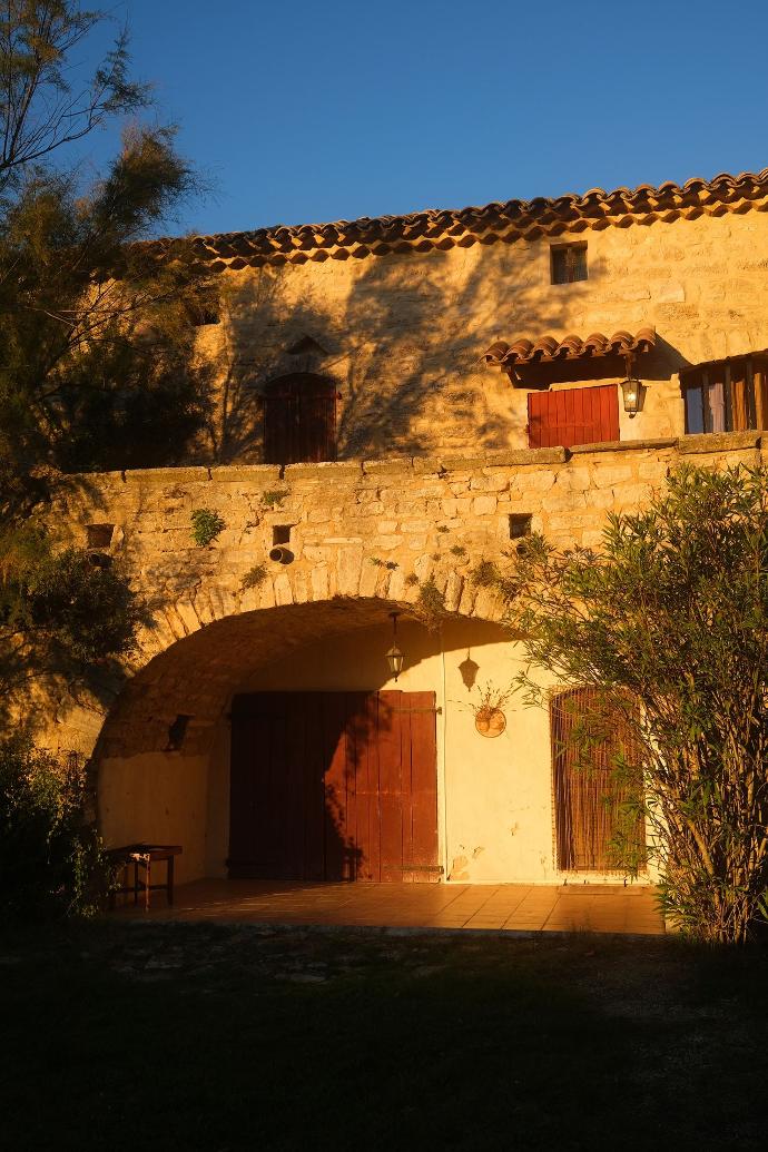 a stone building with red shutters and a bench in front of it