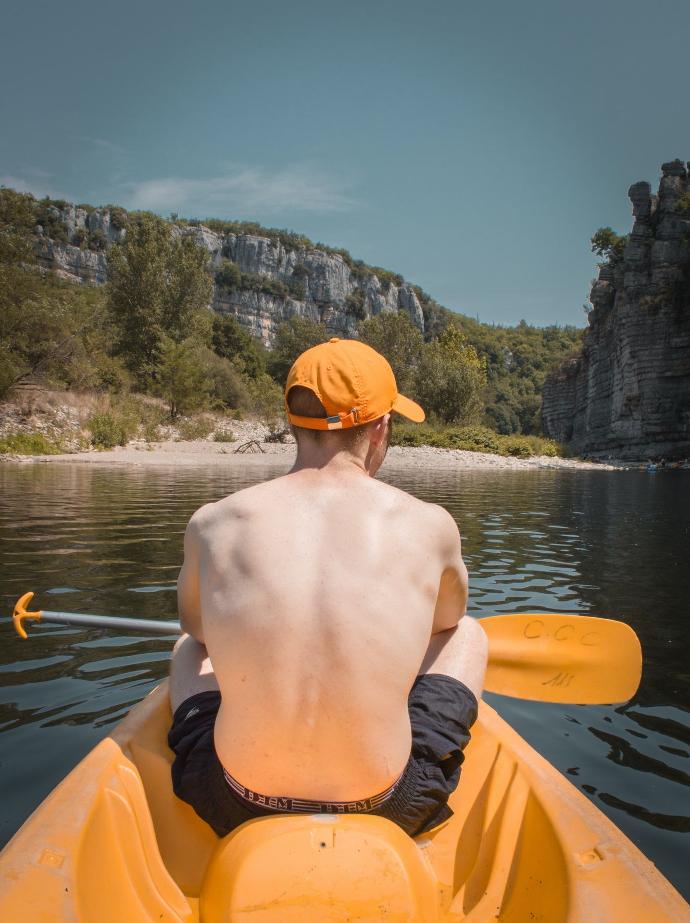topless man wearing orange and black shorts riding orange kayak on lake during daytime