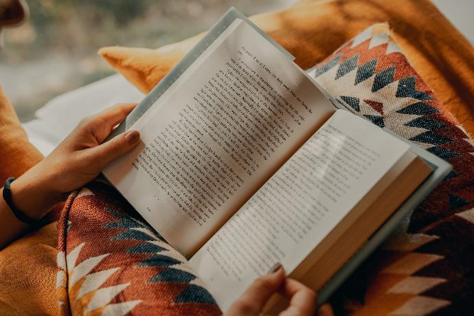 person reading book on brown and beige textile